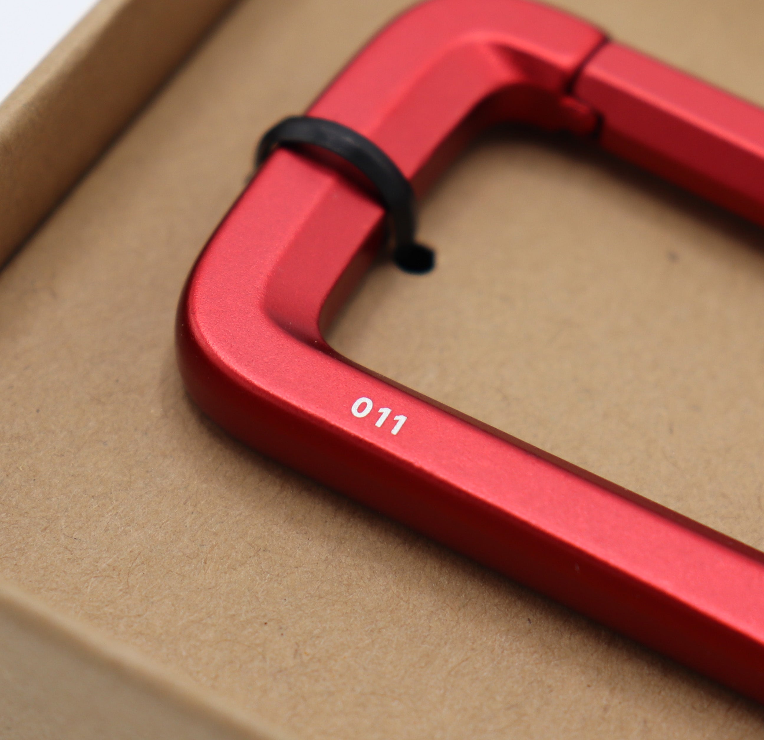Red metal carabiner with '011' engraving on a beige background